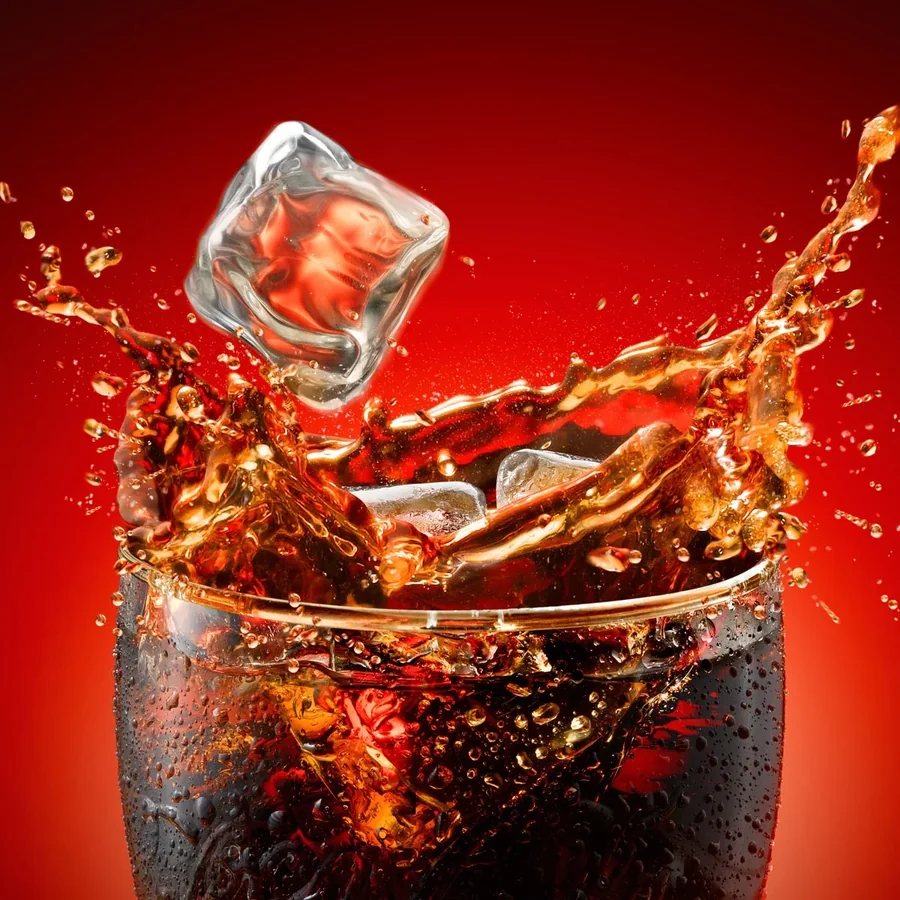A glass of ice-cold cola with ice splashing into it